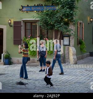 Le petit garçon s'amuse à chasser un pigeon dans les rues pavées de Rothenburg médiéval, tandis que sa mère prend des photos de voyage à l'extérieur de son hôtel. Banque D'Images