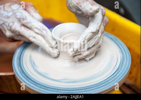 Le potter qui fait des plats de poterie sur tour de potier. Le sculpteur à l'atelier d'argile rend libre. Les mains de potter. Banque D'Images