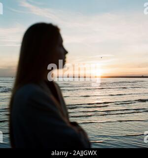 Belle femme debout près de la mer et profitant du coucher du soleil Banque D'Images