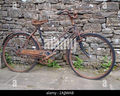 Vieux rouillé pousser/pédaler vélo appuyé contre le mur de pierre sèche avec végétation qui pousse autour Banque D'Images