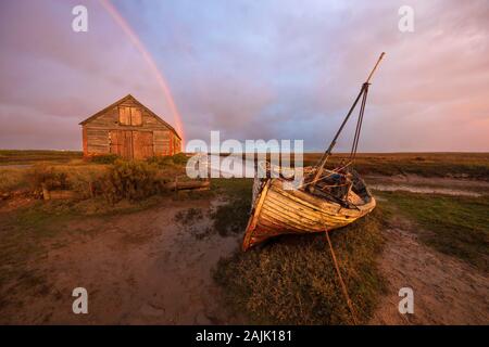 Épave de bateau et d'un hangar à bateaux à Thornham Vieux Port avec rainbow au lever du soleil, Thornham, Norfolk, Angleterre, Royaume-Uni, Europe Banque D'Images