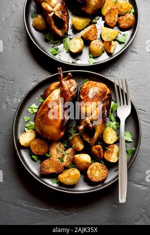 Les carcasses de cailles grillées savoureuses avec pommes de terre au four sur plaque sur fond noir en noir. Banque D'Images