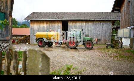 Tracteur tirant le réservoir d'eau dans une enceinte de ferme dans la campagne bavaroise, Allemagne. Banque D'Images