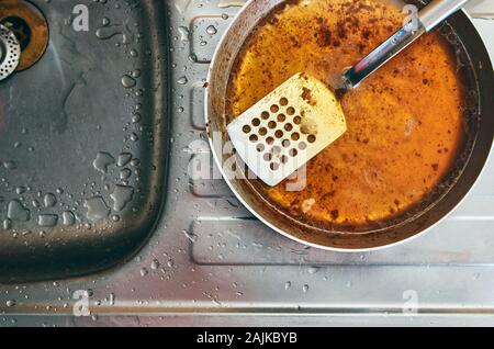 Gras sale carter acier perforé avec spatule. Placé sur le dessus d'un évier de cuisine en acier avec des gouttelettes d'eau tout autour de Banque D'Images
