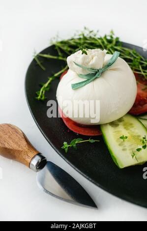 Fromage burrata italien frais avec les tranches de tomate sur une plaque noire sur un fond blanc. Focus sélectif. Une saine nourriture italienne. Banque D'Images