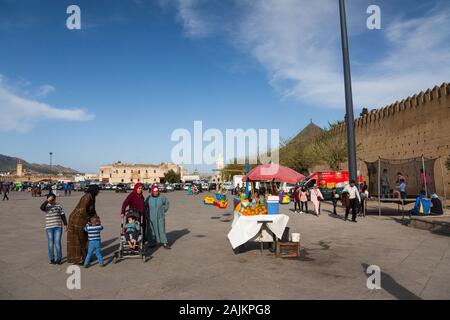 Traditionnellement vêtues de femmes avec des enfants, s'étaler avec des oranges et des enfants jouant sur le carrousel et le trampoline sur La Place Boujloud à Fes (Fez), au Maroc Banque D'Images