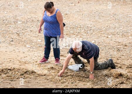 Vieil homme creuser dans le sable d'une plage avec son associé à la recherche sur Banque D'Images