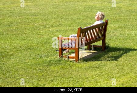 Vieille dame sur un banc de parc le soleil brille, Banque D'Images