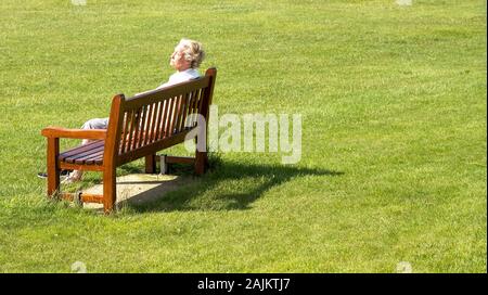 Vieille dame sur un banc de parc le soleil brille, Banque D'Images