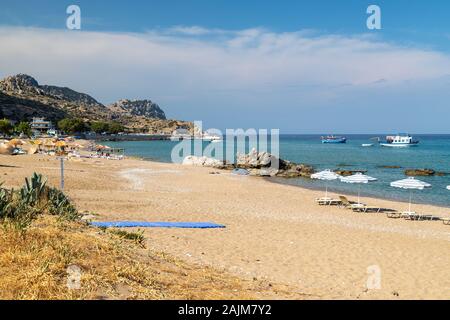 Stegna Beach sur l'île grecque de Rhodes avec du sable, des parasols et bateaux en arrière-plan sur une journée ensoleillée au printemps Banque D'Images