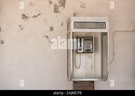 L'utilisation publique paye Vintage cabine téléphonique avec bouton métallique téléphone sur mur déchiqueté blanc Banque D'Images