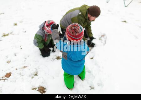 Père faisant un boule de neige dehors avec deux enfants pendant l'hiver Banque D'Images