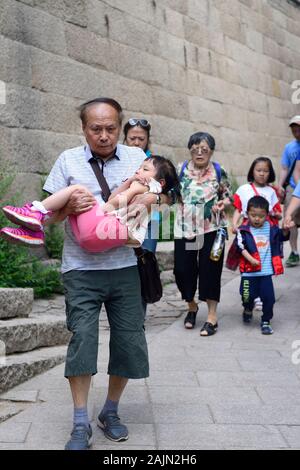 Un grand-père porte son fatigué, jeune petite-fille sur une sortie en famille au site de Badaling de la Grande Muraille de Chine. Banque D'Images