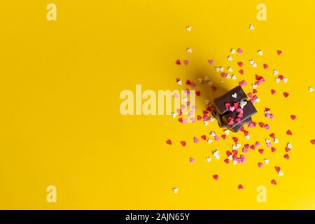 Une pile de chocolats sur un arrière-plan de confettis à partir de petits coeurs. fond jaune. Banque D'Images