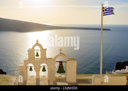 Clocher et le drapeau national de la Grèce dans la lumière au coucher du soleil à Oia, Santorin, Grèce Banque D'Images