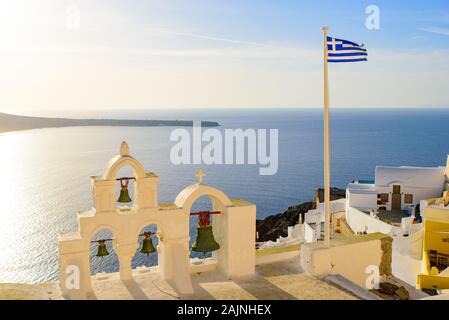 Clocher et le drapeau national de la Grèce dans la lumière au coucher du soleil à Oia, Santorin, Grèce Banque D'Images