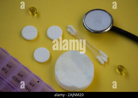 Tas de comprimés et gélules, box pour le stockage des médicaments et du matériel médical stéthoscope et compteur de pression sur fond jaune, les soins de concept Banque D'Images