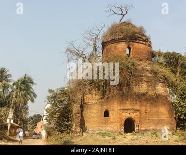 Bishnupur, Bengale de l'Ouest, Inde - 6 février 2018 : une ruine surcultivée d'un vieux temple de briques construit par la dynastie Malla. Les enfants font du vélo sur la route que goe Banque D'Images