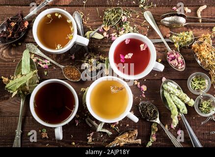 Assortiment de tasses de thé sec et en t dans une cuillères sur fond de bois. Vue d'en haut. Banque D'Images