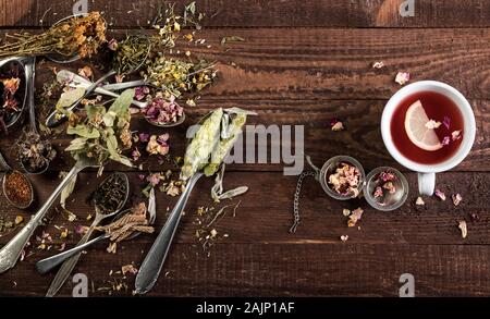 Assortiment de thé sec dans des cuillères et tasse de thé sur fond de bois. Vue de dessus avec l'exemplaire de l'espace. Banque D'Images