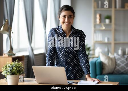 Happy indian girl looking at camera at home with laptop Banque D'Images