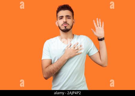 Je le promets. Portrait d'homme avec barbe brune grave en t-shirt blanc debout avec bras soulevé, jurant allégeance, avec serment ex responsable Banque D'Images