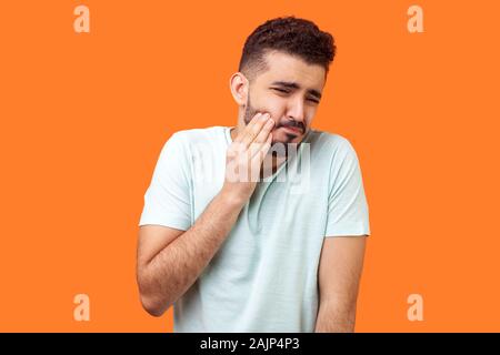 Problème dentaire. Portrait d'homme avec barbe brune malsaine en t-shirt blanc, sur sa joue et grimaces de terribles maux, sensible tee Banque D'Images