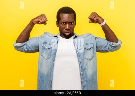 Je suis fort ! Portrait de confiance en eux-mêmes motivés jeune homme en denim chemise décontractée à la collecte d'assurance et d'armes pour montrer les biceps, sentiment puissant. Banque D'Images