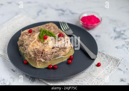 Gelée de viande, de porc et de poulet, l'aspic. Un plat traditionnel russe, servant sur une assiette, à côté le raifort dans un bol. Sur un fond gris sous Banque D'Images