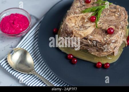 Gelée de viande, de porc et de poulet, l'aspic. Un plat traditionnel russe, servant sur une assiette, à côté le raifort dans un bol. Sur un fond gris sous Banque D'Images