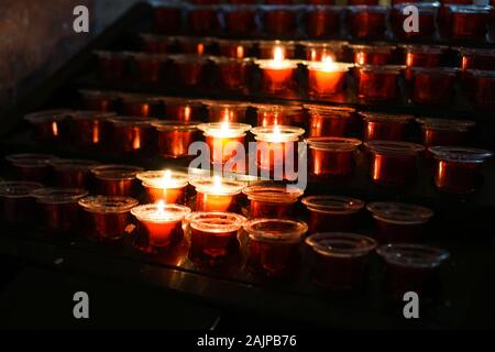 Rangées de bougies allumées dans une église dim Banque D'Images