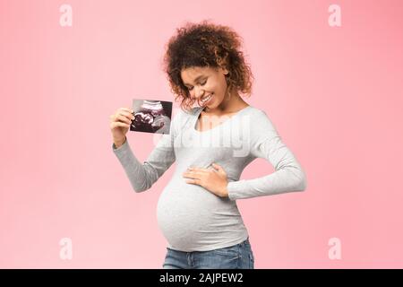 Première échographie. Future mère holding échographie et de toucher son ventre, sur fond rose Banque D'Images