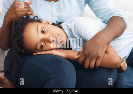 Soutien à la famille. Femme noire la réconforter offensé gamin qui ment sa tête sur les genoux de mère Banque D'Images