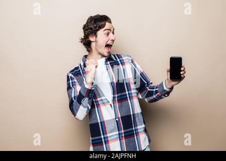 Portrait d'un jeune homme excité isolés sur fond beige, holding mobile phone Banque D'Images