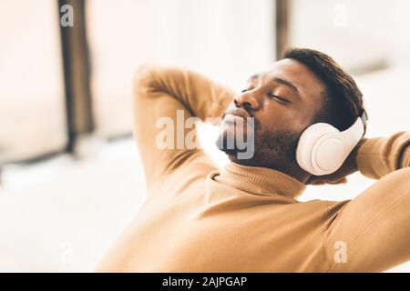 Le temps de vous détendre. L'homme afro satisfaits dans les écouteurs profiter de la musique avec les yeux fermés, se penchant en arrière dans office, de l'espace libre Banque D'Images