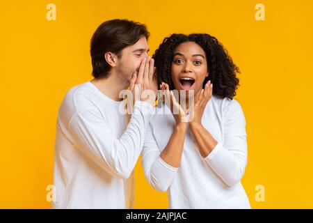 Jeune homme secret partage avec sa petite amie noire, le commérage ensemble au fond jaune avec de l'espace libre Banque D'Images