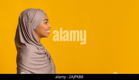 Profile portrait of smiling black femme musulmane en foulard à la copie à l'espace sur fond jaune, panorama Banque D'Images