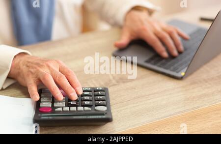 Libre d'un homme âgé's Hands Calcul Finances publiques à l'aide de la calculatrice et Laptop Sitting in Office. Cropped Banque D'Images