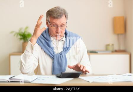 Angry Man Calcul de factures et impôts à la calculatrice en faisant des gestes avec les mains assis à un bureau à l'intérieur. Selective Focus Banque D'Images