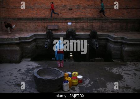 Kathmandu, Népal. 5Th Jan, 2020. Une femme remplit l'eau comme les enfants jouent à un diffuseur d'eau historique à Kathmandu, Népal le Dimanche, Janvier 5, 2020. Credit : Skanda Gautam/ZUMA/Alamy Fil Live News Banque D'Images