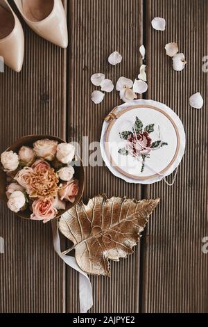 Rose et de pivoines fleurs dans une boîte ronde, les anneaux de mariage sur la feuille d'or, suite nuptiale sur chaussures hauts talons sur fond de bois, vue du dessus. Détails de mariage Banque D'Images