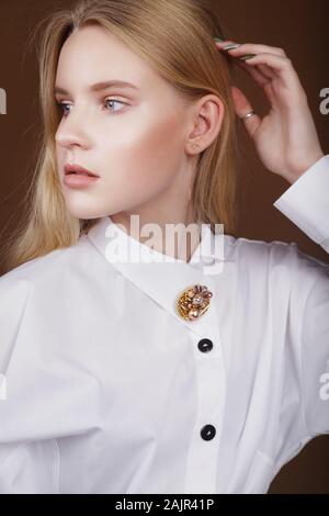 Belle jeune fille blanche close-up dans un costume blanc avec broche broche fait main, accessoire en studio. Boutique de mode, publicité, magazine, bijoux Banque D'Images