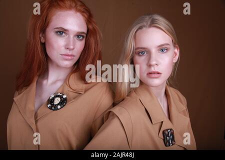 Fermer portrait de deux belles jeunes filles avec les produits de maquillage, vêtu de vêtements beige sur un fond brun. Accessoire de mode et concept. Les jeunes Banque D'Images