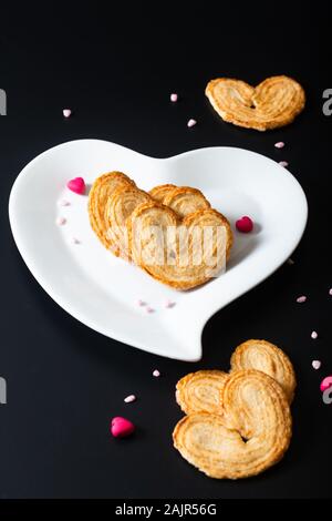Concept alimentaire dessert Saint Valentin coeurs de pâte feuilletée en forme de coeur en céramique blanche sur fond noir avec copie espace Banque D'Images