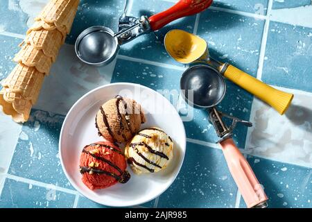 Servant de la crème glacée à saveur différente avec trois boules et cornets ou cônes gaufrette sur fond de carrelage bleu Banque D'Images