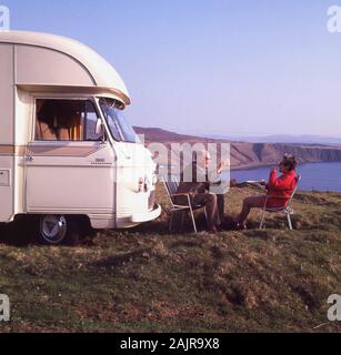 Années 1970, Cheers ! Un couple de retraités levez votre verre à la santé de chacun, comme ils sont assis à l'extérieur de leur commer campervan, un 'Jennings 2500 Roadranger', sur la côte à côté d'une plage de sable fin sur l'île de South Uist, dans les Hébrides extérieures dans les Highlands, Ecosse, Royaume-Uni. Banque D'Images