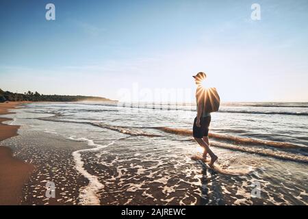 Jeune homme avec sac à dos marche sur la plage de sable tropicale. Côte du Sri Lanka au lever du soleil. Banque D'Images