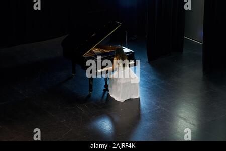 Une femme avec les cheveux bruns habillé en robe blanche vu jouer un piano à queue noir avec le couvercle soulevé. Vue de dessus de la pianiste Banque D'Images