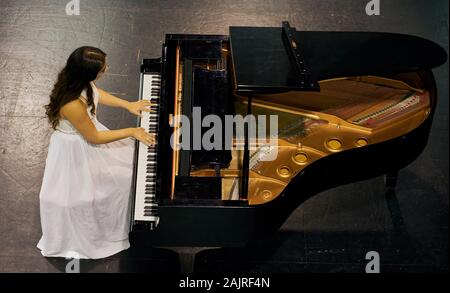 Une femme avec les cheveux bruns habillé en robe blanche vu jouer un piano à queue noir avec le couvercle soulevé. Vue de dessus de la pianiste Banque D'Images