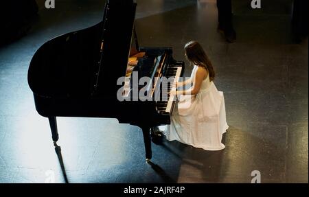 Une femme avec les cheveux bruns habillé en robe blanche vu jouer un piano à queue noir avec le couvercle soulevé. Vue de dessus de la pianiste Banque D'Images